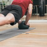 Una persona, dentro de un gimnasio, realizando flexiones apoyado sobre un balón medicinal