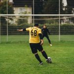 Un jugador chutando un balón a un portero.