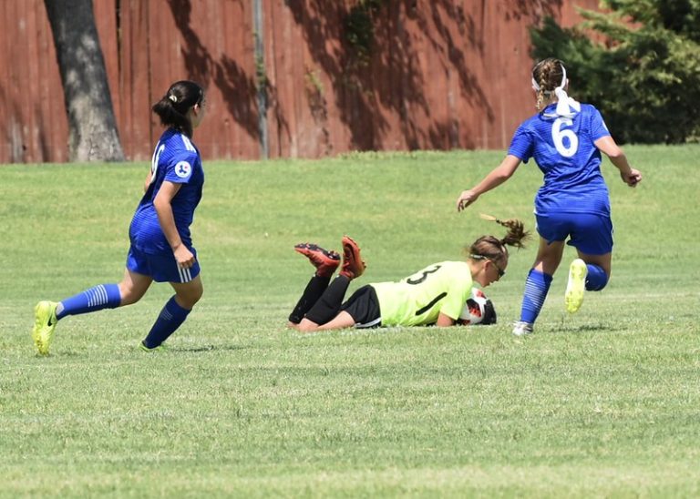 Una portera de fútbol realizando una parada frontal rasa con caida.